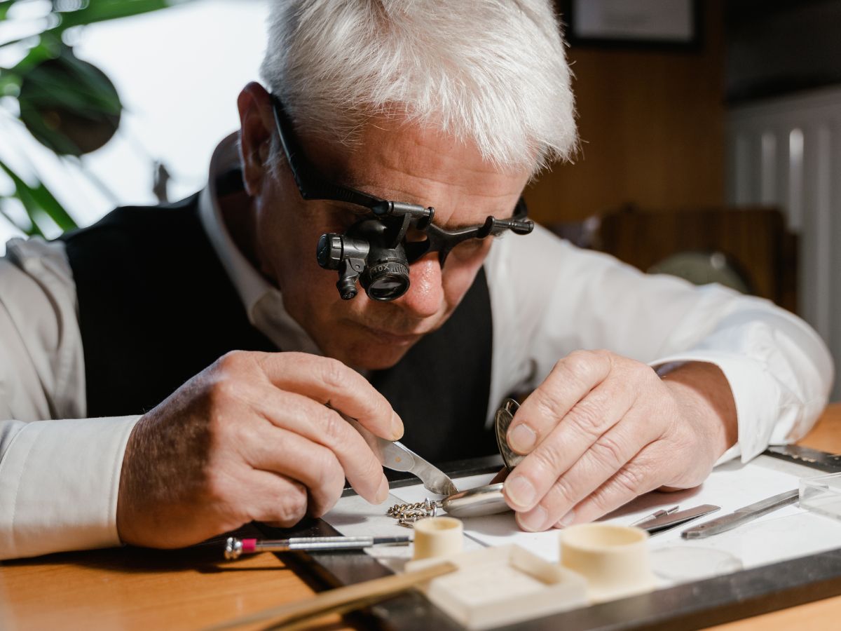 An older man carefully repairs a watch, focusing intently on the intricate mechanisms and tools in front of him.
