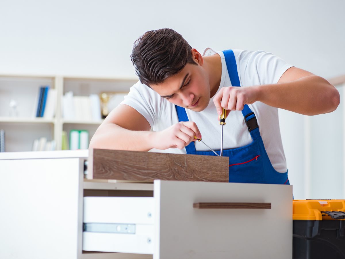 A man wearing an apron is focused on crafting a wooden cabinet in a workshop setting.