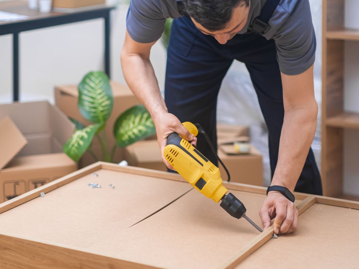 A man uses a power drill to assemble furniture, focused on his task in a well-lit workshop.